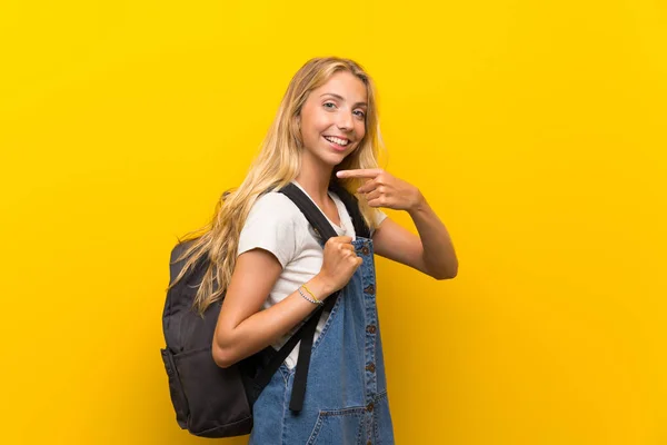 バックパックと孤立した黄色の背景の上にブロンドの若い女性 — ストック写真
