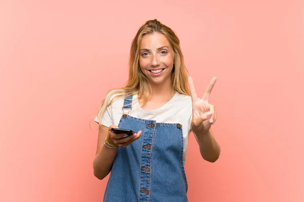 Blonde Jonge Vrouw Met Een Mobiele Telefoon Geïsoleerde Roze Muur — Stockfoto