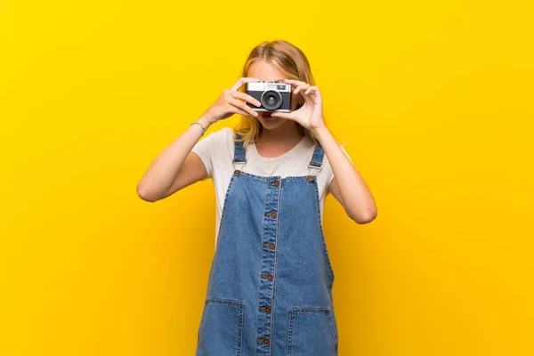 カメラを持つ孤立した黄色の背景の上にブロンドの若い女性 — ストック写真