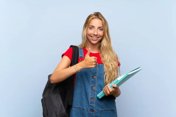 Young blonde student woman over isolated blue wall giving a thumbs up gesture