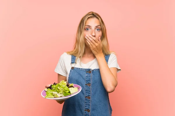 Blonde young woman with salad over isolated pink wall with surprise facial expression