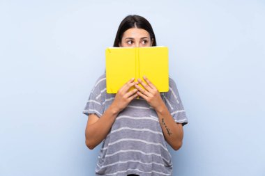 Izole mavi arka plan üzerinde genç esmer kadın tutma ve bir kitap okuma