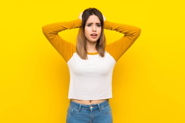 İzole sarı duvar üzerinde güzel genç kadın sinirli ve kafasına eller alır