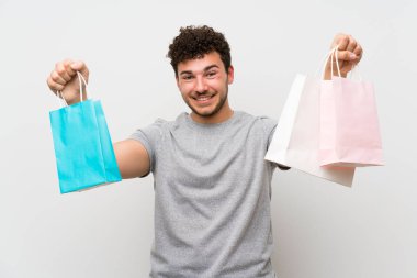 Bir sürü alışveriş poşeti tutan izole duvarın üzerinde kıvırcık saçlı adam