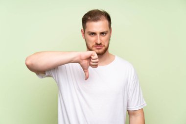 Yeşil arka planda yakışıklı adam başparmak aşağı işareti gösteren