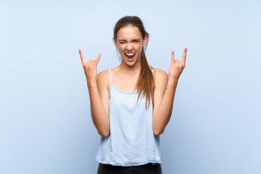 Izole mavi arka plan üzerinde rock jest yapma genç kadın