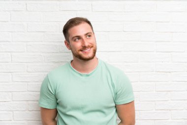 Tuğla duvar üzerinde sarışın adam gülüyor ve bakıyor