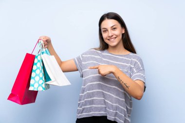Alışveriş torbaları bir sürü tutan izole mavi arka plan üzerinde genç esmer kadın