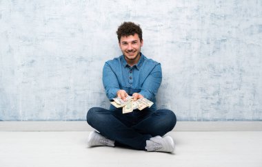 Yerde oturan ve çok para alan genç adam.