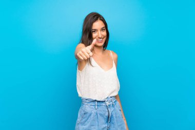 Soyutlanmış mavi arka planı olan genç bir kadın. Başparmakları havada çünkü iyi bir şey oldu.