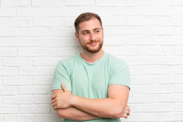 Blonde man over brick wall standing and looking to the side