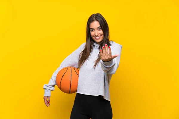 年轻女子在孤立的黄色背景上打篮球 邀请她来 很高兴你来了 — 图库照片