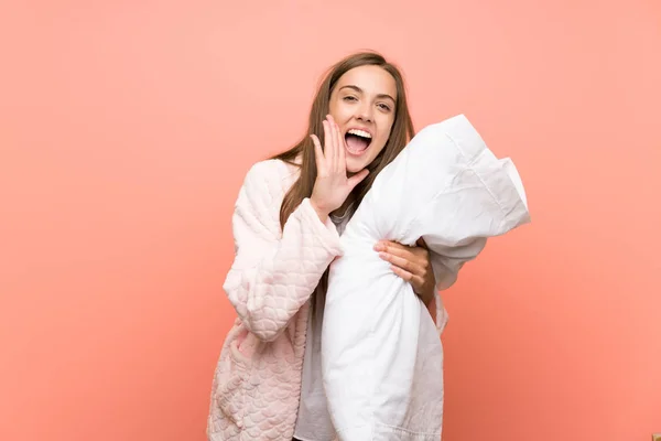 Young woman in dressing gown over pink wall shouting with mouth wide open