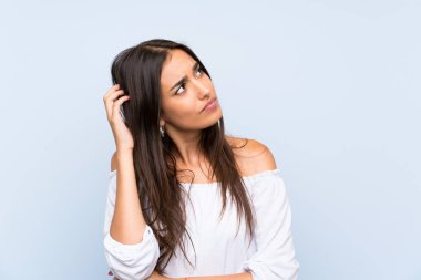 Soyutlanmış mavi arka planı olan genç bir kadın. Şüpheleri var ve kafası karışık.