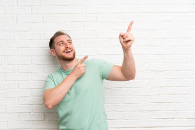 Tuğla duvar üzerinde sarışın adam indeks parmak büyük bir fikir ile işaret