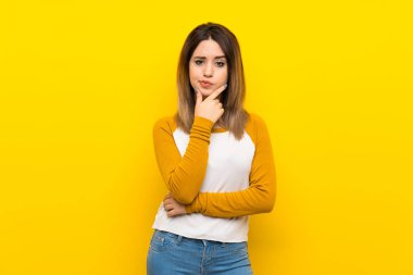 İzole sarı duvar düşünme üzerinde güzel genç kadın