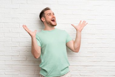 Sürpriz yüz ifadesi ile tuğla duvar üzerinde sarışın adam