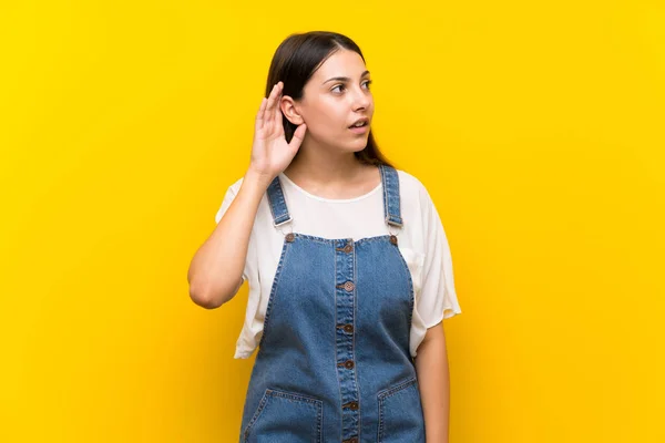 Jovem Mulher Dungarees Sobre Fundo Amarelo Isolado Ouvir Algo Colocando — Fotografia de Stock