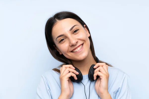Молодая женщина слушает музыку на изолированном синем фоне — стоковое фото
