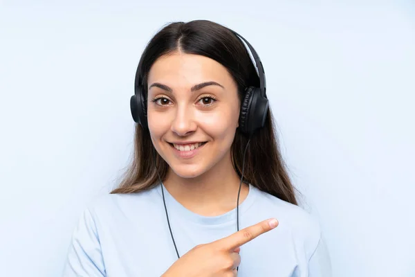 Молодая Женщина Слушает Музыку Изолированном Синем Фоне Указывая Сторону Представить — стоковое фото