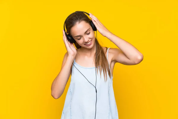 Mladá žena naslouchající hudbě přes izolované žluté nástěnné zpívání — Stock fotografie