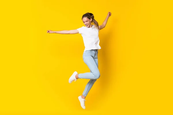 Mladá žena skákající přes izolovanou žlutou zeď — Stock fotografie
