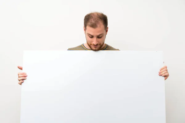 英俊的男人在孤立的白色墙壁上拿着一个空的白色标语牌插入一个概念 — 图库照片