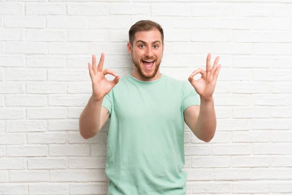 Blonde Man Bakstenen Muur Toont Een Teken Met Vingers — Stockfoto