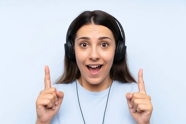 Jovem Mulher Ouvindo Música Sobre Fundo Azul Isolado Apontando Para — Fotografia de Stock