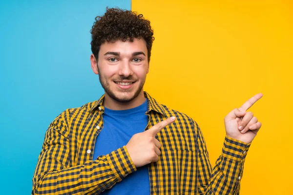 Man Curly Hair Colorful Wall Pointing Finger Side — Stock Photo, Image