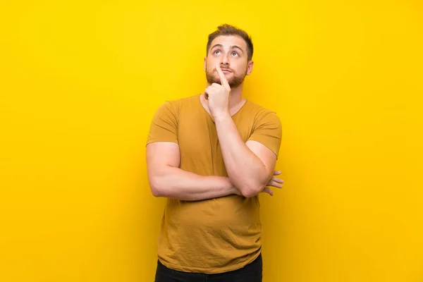 Blonde man over isolated yellow wall thinking an idea pointing the finger up