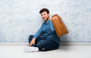Yerde oturan genç adam elinde vintage bir çantayla