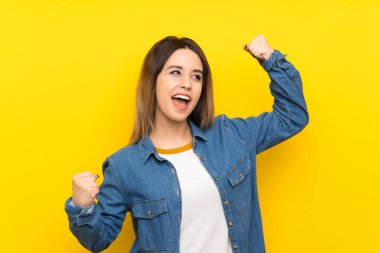 Sarı arka plan üzerinde genç kadın bir zafer kutluyor