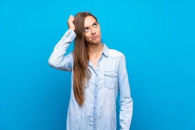 Soyutlanmış mavi arka planı olan genç bir kadın kafasını kaşırken şüpheye düşüyor.
