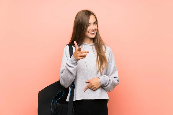 Young sport woman over isolated pink background points finger at you