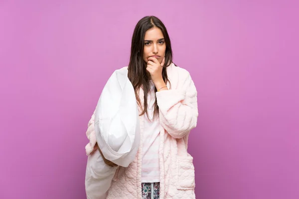 Young woman in pajamas and dressing gown over isolated purple background thinking an idea