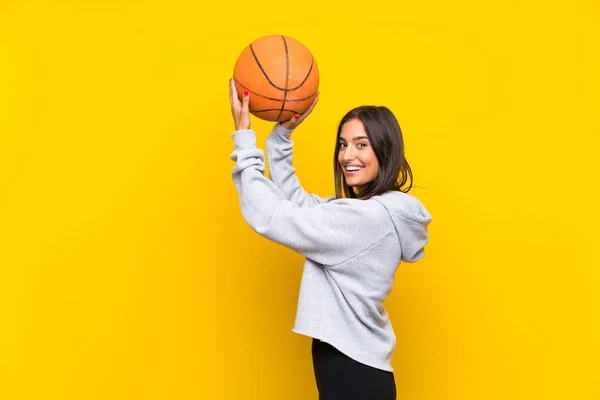 Wanita muda bermain basket melalui latar belakang kuning yang terisolasi — Stok Foto