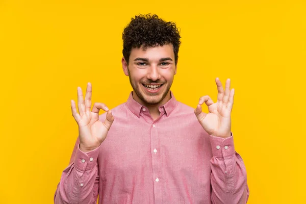 Człowiek Kręcone Włosy Nad Białym Żółtym Ścianie Pokazując Znak Palcami — Zdjęcie stockowe