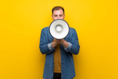 Bir megafon üzerinden bağıran izole sarı duvar üzerinde sarışın adam