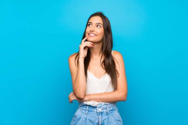 Soyutlanmış mavi arka planda genç bir kadın yukarı bakarken bir fikir düşünüyor.