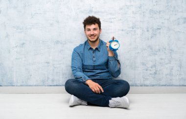 Genç adam vintage çalar saat tutarak katta oturan