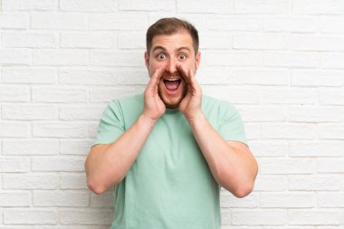 Sarışın adam üzerinde tuğla duvar çığlık ile ağız geniş açık