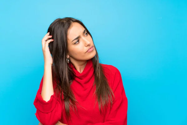 孤立した青い背景の上に赤いセーターを持つ若い女性は 疑問を持ち 顔の表情を混乱させる — ストック写真