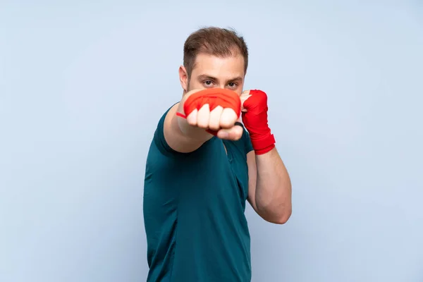 Blonde sport man over blue wall in boxing bandages — Stock Photo, Image