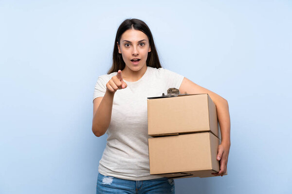 Young delivery woman over blue brick wall surprised and pointing front