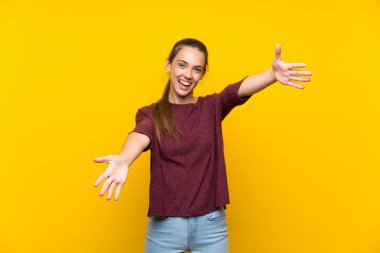Izole sarı arka plan üzerinde genç kadın sunan ve el ile gelmek için davet