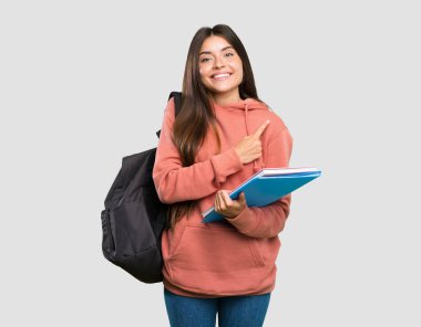 İzole gri arka plan üzerinde bir ürün sunmak için yan işaret defterleri tutan genç öğrenci kadın