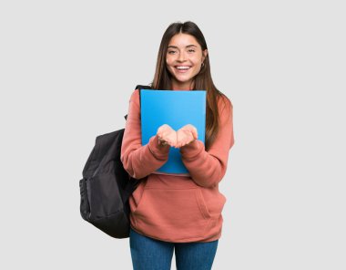 İzole gri arka plan üzerine bir reklam eklemek için avuç içinde taklit alanı hayali tutan deftertutan genç öğrenci kadın