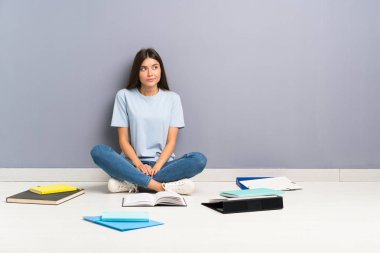 Yerde ayakta ve yan bakarak birçok kitap ile genç öğrenci kadın