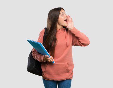 Genç öğrenci kadın izole gri arka plan üzerinde lateral ağız ardına açık bağırarak defter tutan